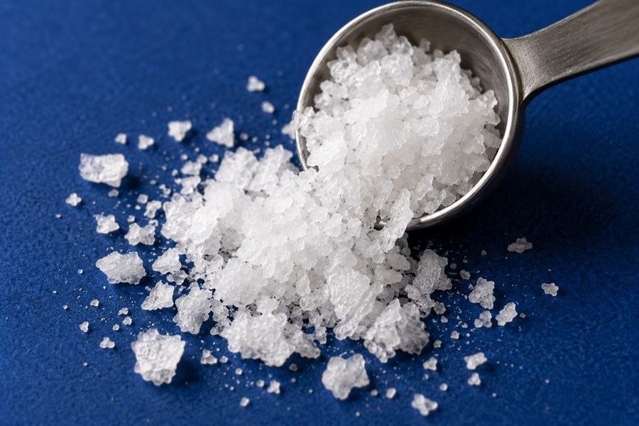 White salt crystals in a measuring spoon on a blue surface
